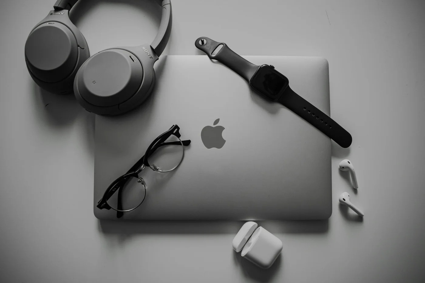 Headphones, a laptop, a watch and glasses on a desk